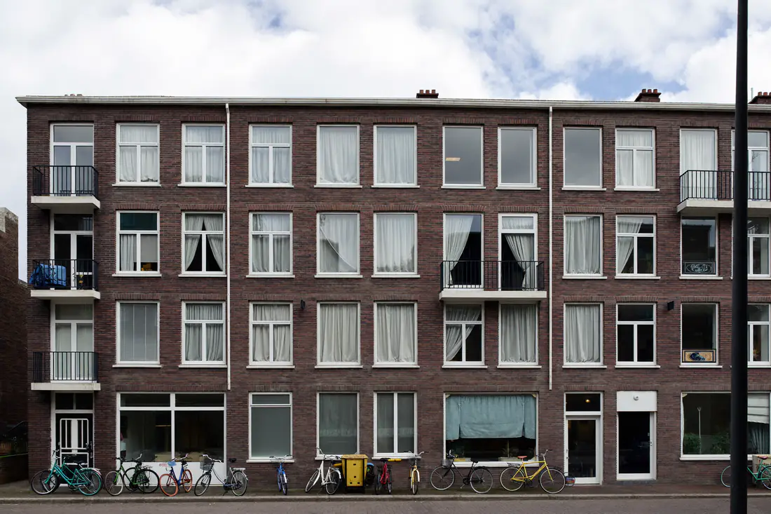 Bakstenen appartementengebouw uit de jaren zeventig met rijen ramen en balkons, fietsen voor de deur