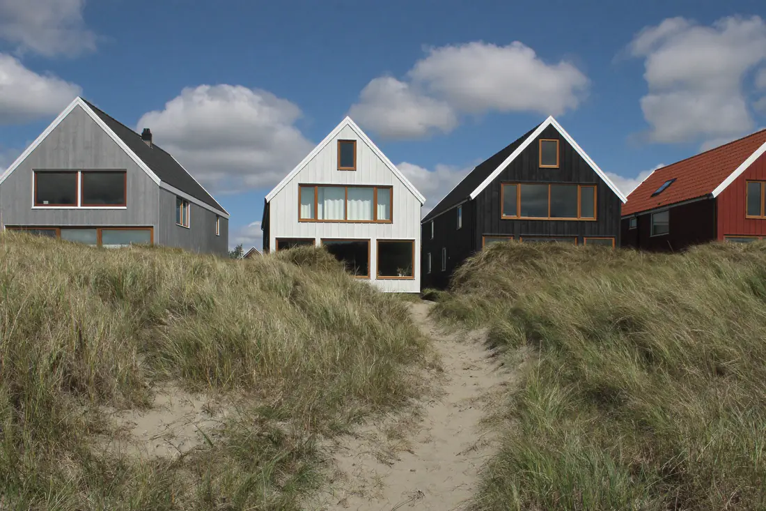 Houten huizen achter de duinen in een Noord-Hollands kustdorp met helmgras op de voorgrond