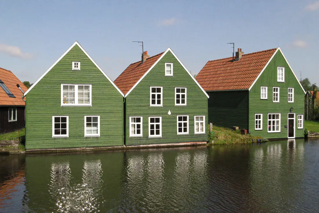 Groen geschilderde houten huizen met witte kozijnen aan het water in de Zaanstreek