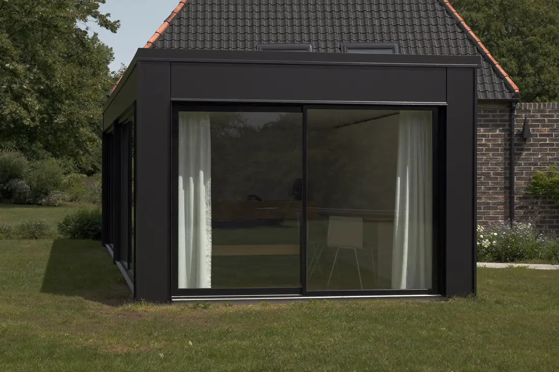 Slanke zwarte aluminium kozijnen en schuifdeuren in een moderne uitbouw aan de achterkant van een woning